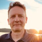 A picture of Peter Scott, a man with dark hair, at sunset on a beach.