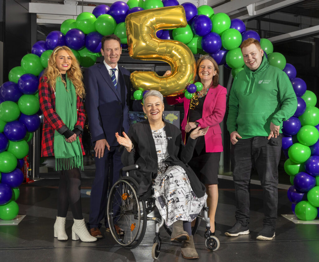 Photocall of Transition Fund event guests in front of gold 5 balloon and green and purple balloons.