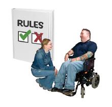 A woman kneels to talk to a man in a wheelchair. Behind them is a rule book with the words Rules on it and a green check and red cross on it.