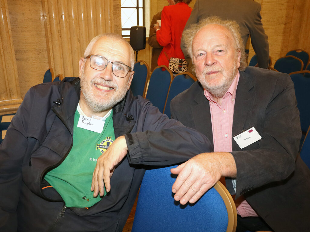 Two men, seated, pose for a photograph.