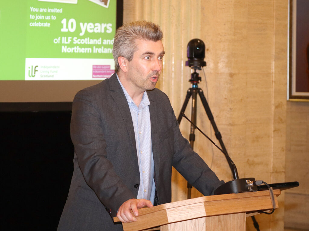 A man (MLA Danny Donnelly) stands at the podium.