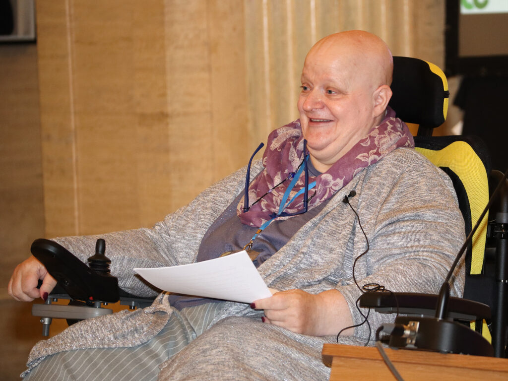 A lady sits, with a smile on her face, holding her speech.