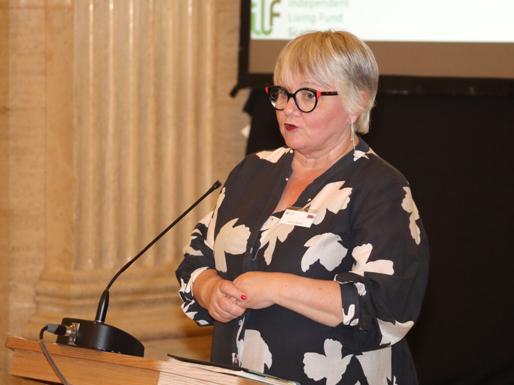 A lady in a floral dress stands at the podium.