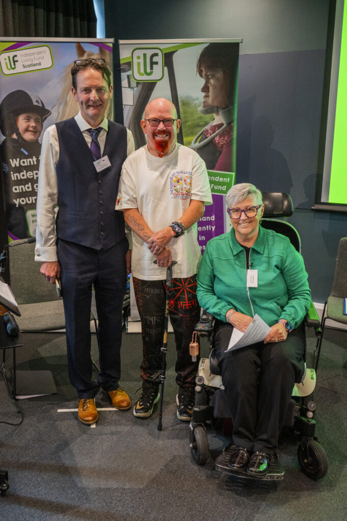 Three people standing and sitting in front of the ILF banner.s