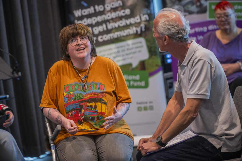 A young lady in an orange top acts with a gentleman in grey.
