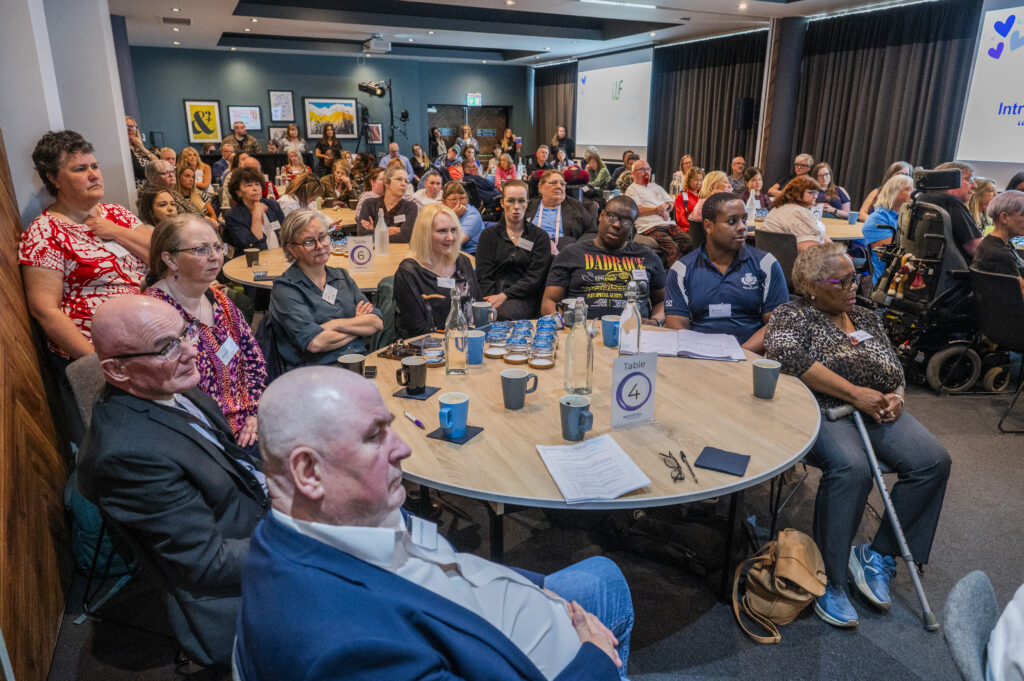 The event room from the front with lots of people sitting at tables.