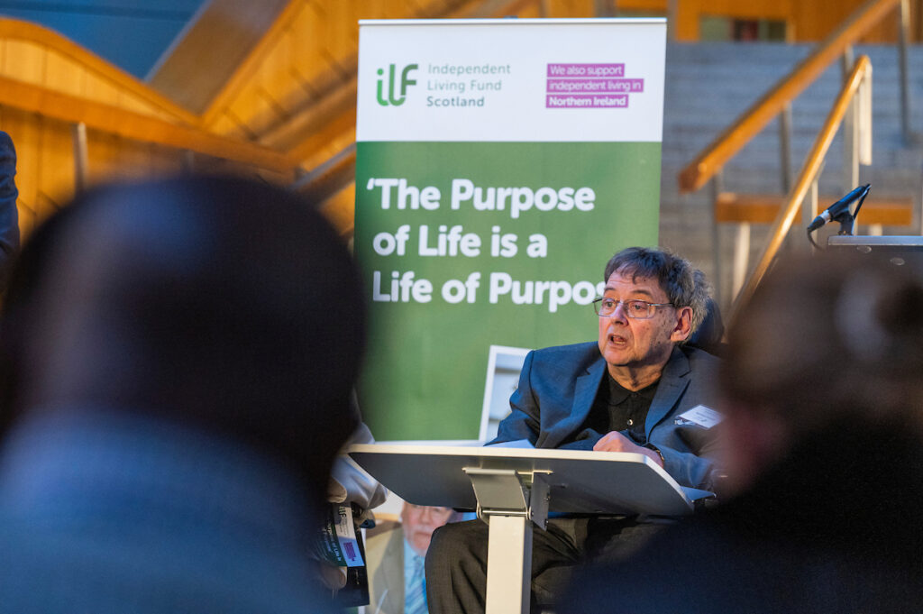 A picture of Etienne speaking at our conference. We are viewing him from the audience and can see blurry heads around us. Behind Etienne is a banner that reads The Purpose of Life is a Life of Purpose.