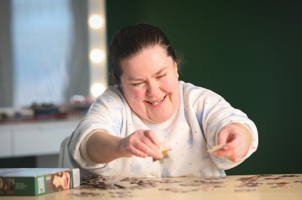 A young lady smiles as she puts together a jigsaw puzzle.