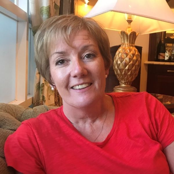 Aileen is pictured in a bright red tshirt and pearl earrings, and has short blonde hair.