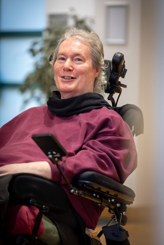 David McDonald in a powered wheelchair, wearing a plum-coloured top, smiling and looking towards the camera.