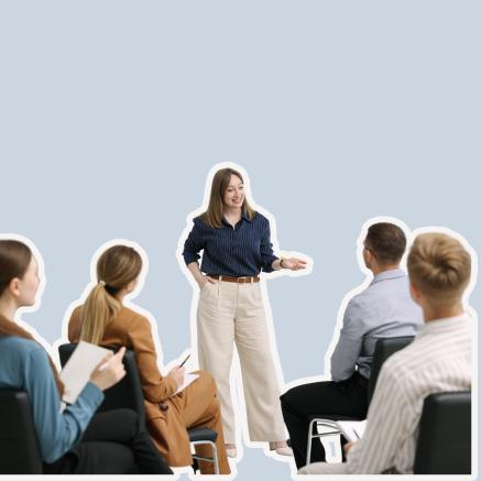 A woman stands at the front of seated people. She's giving a talk.